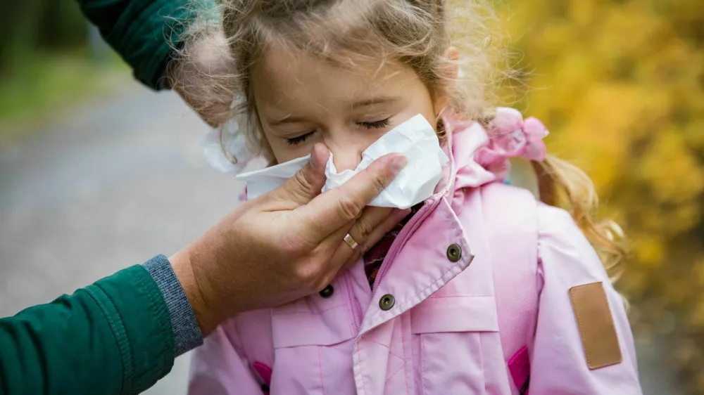 Father wiping daughter's nose with handkerchief. Sick little girl with cold and flu standing outdoors. Preschooler sneezing, coughing, having runny red nose. Autumn street background / Foto: Suzi Media Production