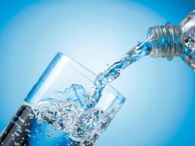 Clear drinking carbonated water pouring into a tall glass from a transparent plastic bottle. Blue backlight, copy space. / Foto: Igorr1