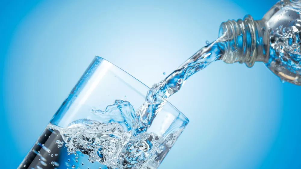 Clear drinking carbonated water pouring into a tall glass from a transparent plastic bottle. Blue backlight, copy space. / Foto: Igorr1