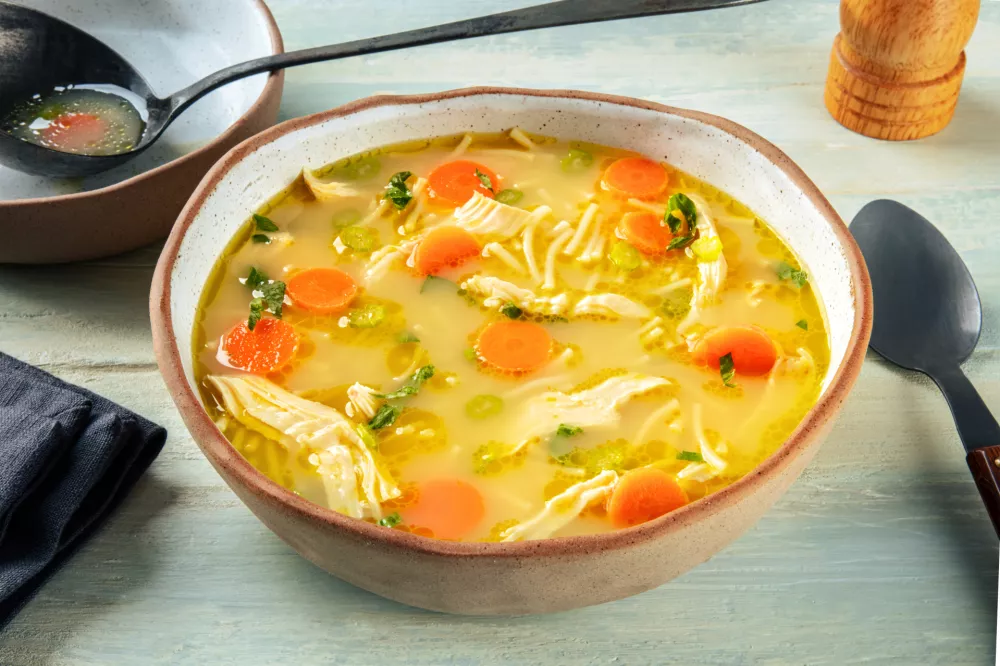 Chicken noodle soup with vegetables, a bowl of healthy broth with a ladle, on a rustic wooden table, winter comfort food / Foto: Cook Shoots Food