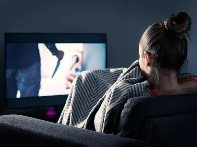 Watching horror and scary film on tv. Woman and thriller movie on television. Person in fear on home sofa couch under blanket at night in dark. Streaming true crime series or halloween show.