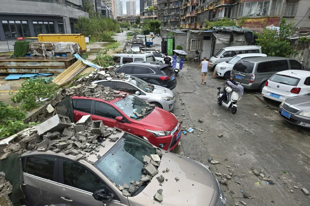 Residents pass by vehicles damaged by a fallen wall in the aftermath of Typhoon Dolphin in Wenzhou in eastern China's Zhejiang province, Monday, Aug. 10, 2026. (Chinatopix via AP)