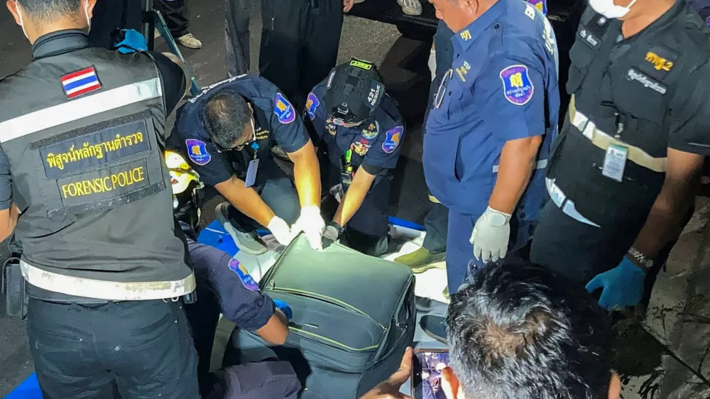 Forensic technicians examine a suitcase, in which police later found the body of a 17-year-old Thai girl, after it was recovered from a grassy area near a railway track in Pattaya City, Thailand, June 27, 2026. Picture taken with a mobile phone. REUTERS/Teerasak Suttativong