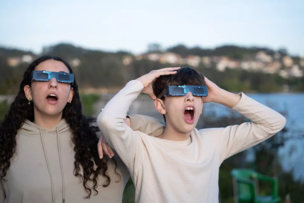 Adolescents observing a solar eclipse using certified protective glasses outdoors. Concept of science, education and safe observation.
