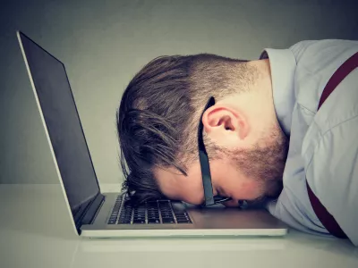 Side view of chubby man looking broken while lying on top of laptop.