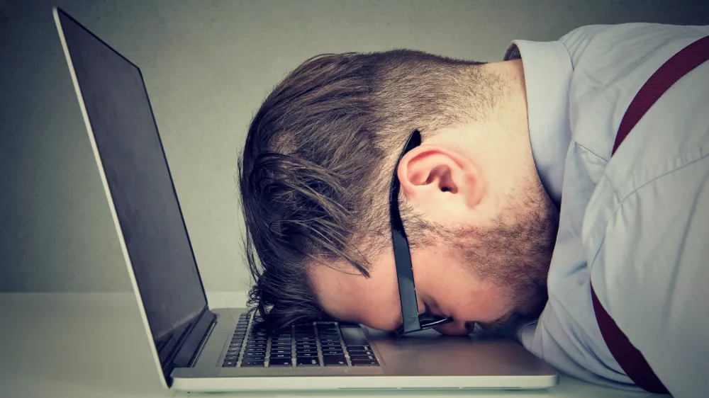 Side view of chubby man looking broken while lying on top of laptop.