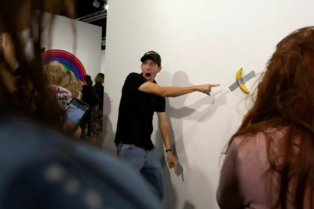 FILE PHOTO: A man poses for a photo next to a banana attached with duct-tape that replaces the artwork 'Comedian' by the artist Maurizio Cattelan, which was eaten by David Datuna, in Miami Beach, Florida, December 7, 2019. REUTERS/Eva Marie Uzcategui/File Photo / Foto: Eva Marie Uzcategui
