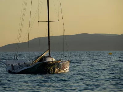 Small sailing yacht floating on gentle waves during golden sunset light. Peaceful seascape with distant mountains and warm evening atmosphere.
