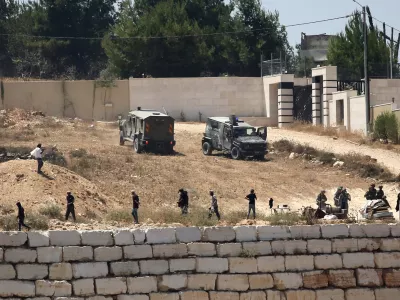 Israeli soldiers stand guard next to settlers in front of Palestinian homes that they have blockaded in the village of Qusra, south of Nablus, in the occupied West Bank, Wednesday, Aug. 12, 2026. (AP Photo/Nidal Eshtayeh)