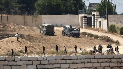 Israeli soldiers stand guard next to settlers in front of Palestinian homes that they have blockaded in the village of Qusra, south of Nablus, in the occupied West Bank, Wednesday, Aug. 12, 2026. (AP Photo/Nidal Eshtayeh)
