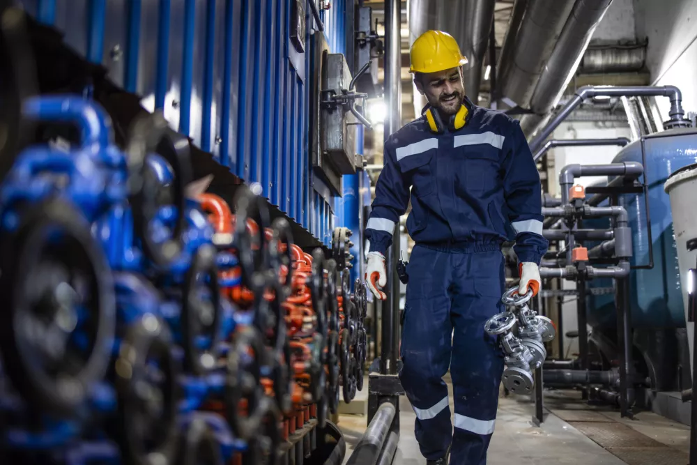 Factory worker replacing high pressure industrial valve in oil refinery.