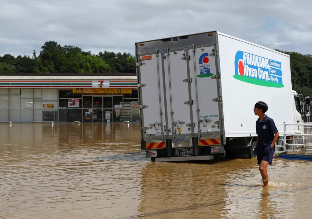 A resident walks near a 7-Eleven store in a flooded area after heavy rain in Oamishirasato, Chiba Prefecture, Japan, August 14, 2026. REUTERS/Issei Kato