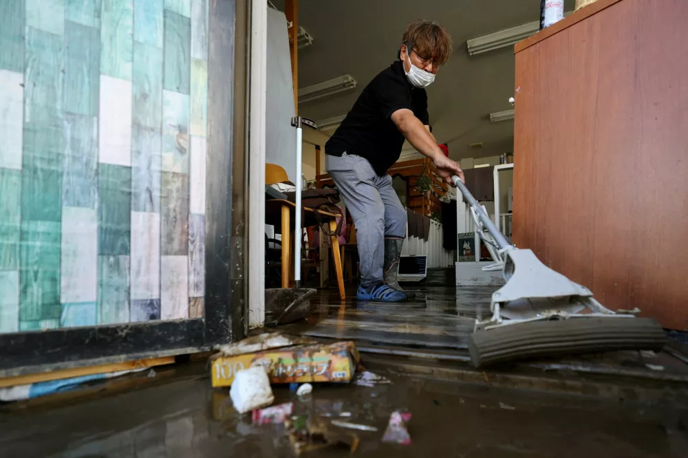 Shinji Fujisawa, 58, a beauty salon owner, clears mud and debris from his house in a flooded area after heavy rain in Oamishirasato, Chiba Prefecture, Japan, August 14, 2026. REUTERS/Issei Kato   TPX IMAGES OF THE DAY