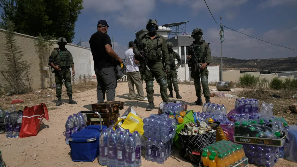 Activists accumulate food and water supplies in front of Israeli army soldiers who are blocking the road leading to the houses of three Palestinian families that have been besieged by Israeli settlers for six days, in the occupied West Bank village of Qusra, south of Nablus, Friday, Aug. 14, 2026. (AP Photo/Majdi Mohammed)
