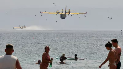 Beachgoers look at the firefighting airplanes scooping water from the Adriatic Sea during a wildfire near Omis, southern Croatia, Friday, Aug. 14, 2026. (AP Photo/Josko Ponos)