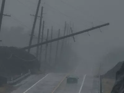 A vehicle drives near a downed utility pole dangling above Mamalahoa Highway during Hurricane Lala near Ocean View, Hawaii, Saturday, Aug. 15, 2026. (Stephen Lam/San Francisco Chronicle via AP)