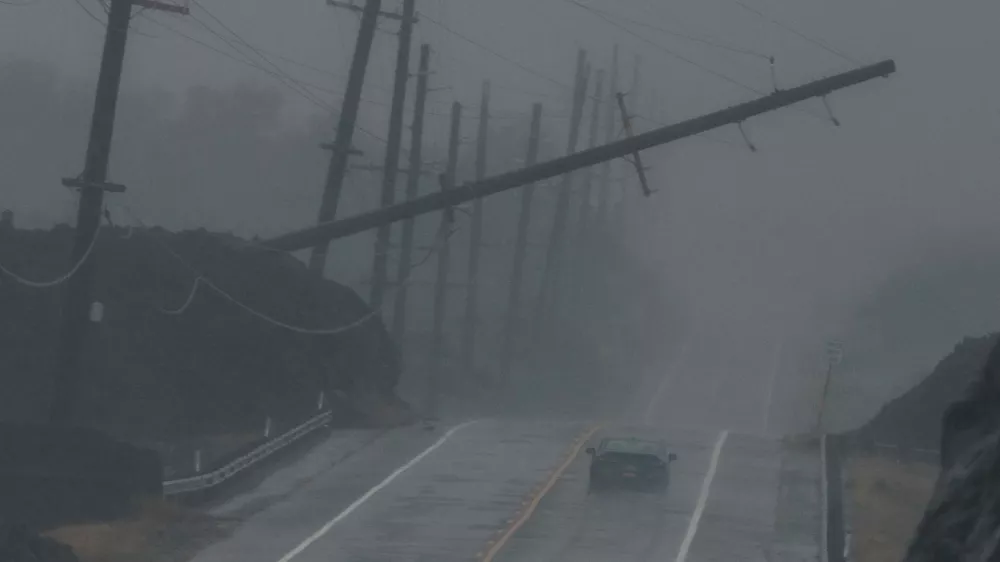 A vehicle drives near a downed utility pole dangling above Mamalahoa Highway during Hurricane Lala near Ocean View, Hawaii, Saturday, Aug. 15, 2026. (Stephen Lam/San Francisco Chronicle via AP)