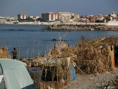 Makeshift shelters used by migrants line the coast as a crowd gathers on a breakwater in Ceuta, Spain, August 15, 2026. REUTERS/Maria Alejandra Cardona