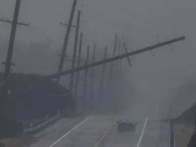 A vehicle drives near a downed utility pole dangling above Mamalahoa Highway during Hurricane Lala near Ocean View, Hawaii, Saturday, Aug. 15, 2026. (Stephen Lam/San Francisco Chronicle via AP)