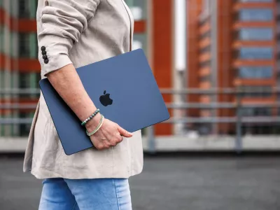Zlin, Czech Republic - April 13, 2025: Businesswoman with Apple laptop MacBook Air walking outside of office building