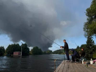 People fish from a pier as smoke billows from the burning Wildberries warehouses following a Ukrainian drone attack, according to the regional governor, in the course of the Russia-Ukraine conflict, in Koledino, Moscow Region, Russia August 16, 2026. Picture taken with mobile phone. REUTERS/Stringer   TPX IMAGES OF THE DAY