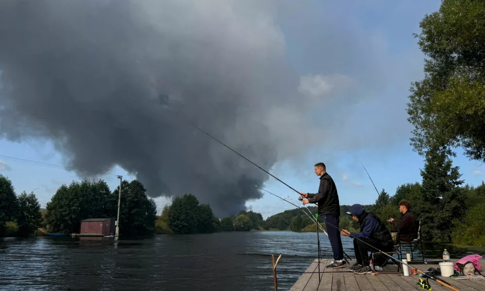 People fish from a pier as smoke billows from the burning Wildberries warehouses following a Ukrainian drone attack, according to the regional governor, in the course of the Russia-Ukraine conflict, in Koledino, Moscow Region, Russia August 16, 2026. Picture taken with mobile phone. REUTERS/Stringer   TPX IMAGES OF THE DAY