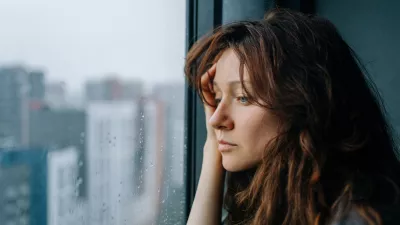 Young woman feeling sad and pensive, experiencing autumn depression while looking out a rainy city window, pondering loneliness and mental health challenges during a melancholic season