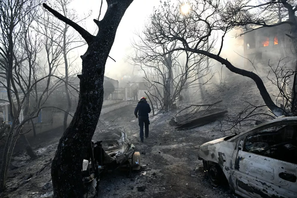 A firefighter walks through a burned area as flames engulf a house during a wildfire on the island of Salamina, west of Athens, Greece, Sunday, Aug. 16, 2026. (AP Photo/Michael Varaklas)