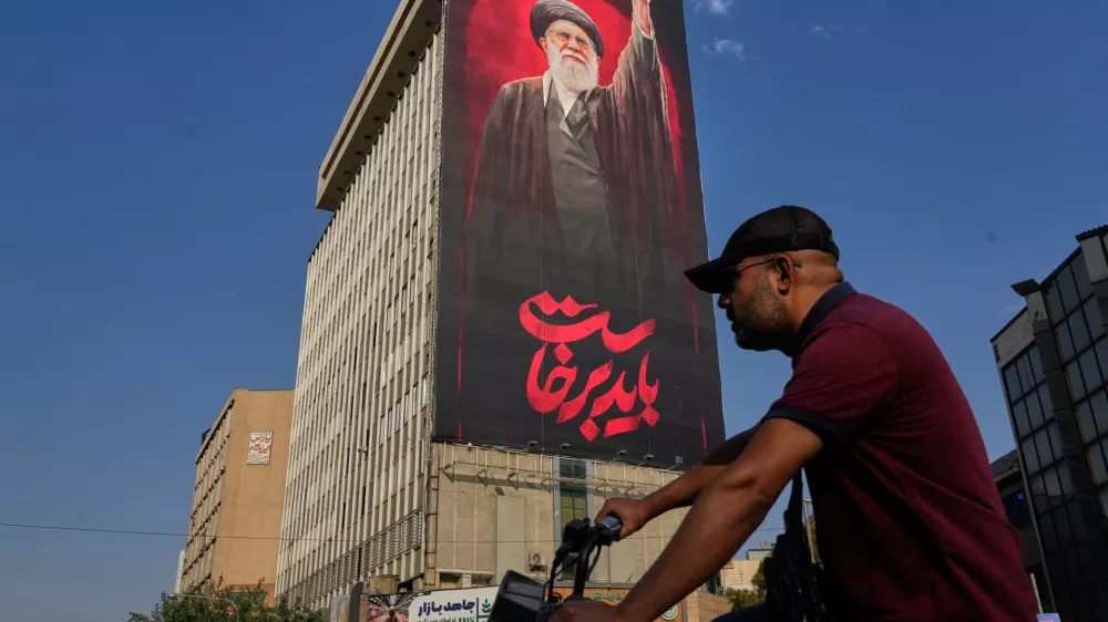 A man rides on his motorbike past a billboard with a message that reads in Farsi: " We must rise up" and an image of the late Iranian Supreme Leader Ayatollah Ali Khamenei, who was killed during the U.S. and Israel strikes on Feb. 28, in Tehran, Iran, Saturday, Aug. 15, 2026. (AP Photo/Vahid Salemi)