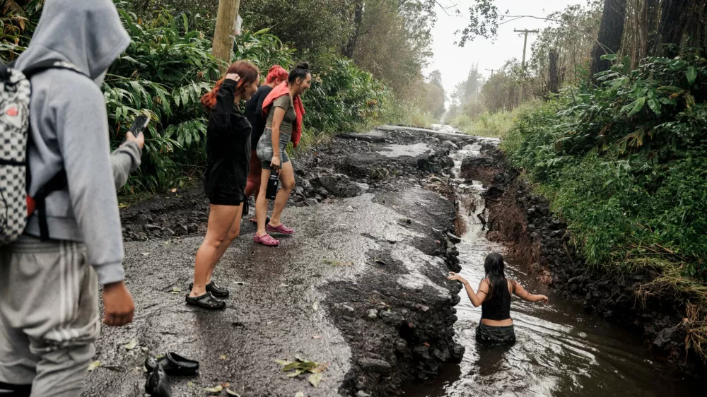 A teenager wades through a pool of water in a washed-out section of a damaged road in Mountain View, Hawaii, Sunday, Aug. 16, 2026, after a severe weather system went through the area. (Stephen Lam/San Francisco Chronicle via AP)