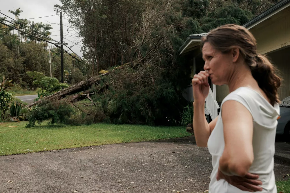 Lenea Masi stands in front of a tree that fell on her home near Volcano, Hawaii, Sunday, Aug. 16, 2026, after a severe weather system went through the area. (Stephen Lam/San Francisco Chronicle via AP)