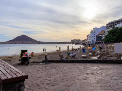 Beach with tourists, sunloungers, sunshades, Atlantic Ocean, hotels and volcanic cone Montana Roja (Red Mountain) at sundown in town El Medano on Canary Island Tenerife, Spain / Foto: Johannes86 Getty Images