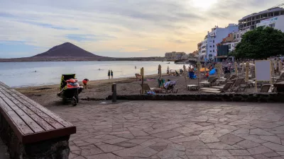 Beach with tourists, sunloungers, sunshades, Atlantic Ocean, hotels and volcanic cone Montana Roja (Red Mountain) at sundown in town El Medano on Canary Island Tenerife, Spain / Foto: Johannes86 Getty Images