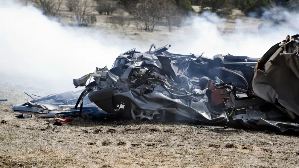 Car run over by a tank on a battlefield. Totally wrecked and smoke still around it. Trees and bushes in the back ground