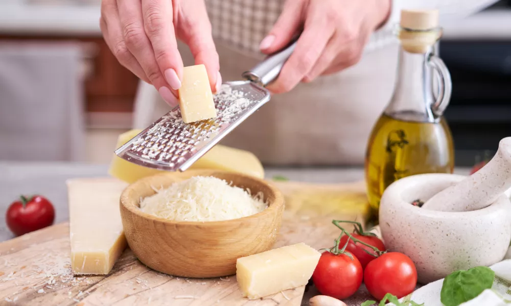 Woman grates Parmesan cheese on a wooden cutting board at domestic kitchen.