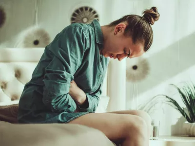 Young woman suffering from PMS and menstruation pain in bedroom at home. Having stomach ache, abdominal pain because of critical days. Inflammation and infection bladder, cystitis