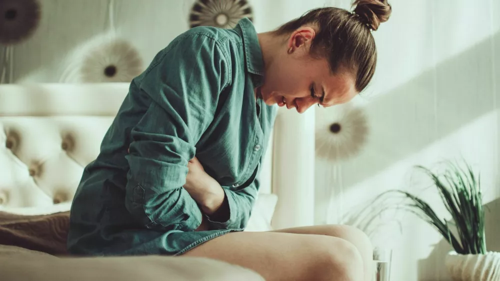 Young woman suffering from PMS and menstruation pain in bedroom at home. Having stomach ache, abdominal pain because of critical days. Inflammation and infection bladder, cystitis