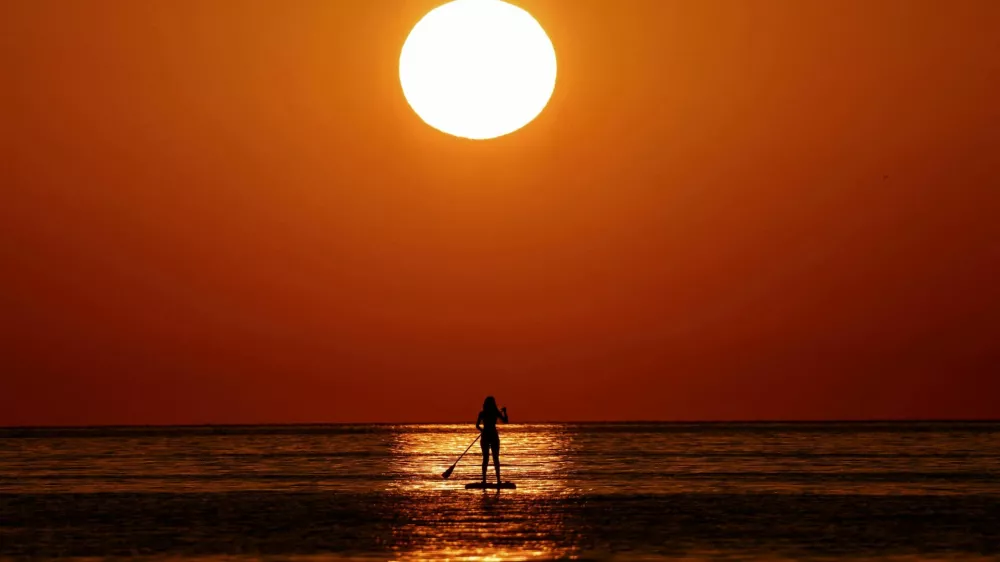 FILE PHOTO: A woman looks at the sunrise as she paddleboards on the Mediterranean Sea, in Barcelona, Spain July 2, 2025. REUTERS/Nacho Doce/File Photo