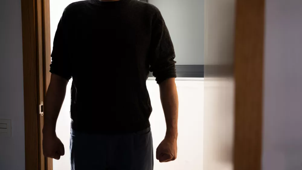 A dark room,a door opens with a silhouette of an unrecognisable man appears, he stands in the doorway and looks at his victim.Focus on shadow.