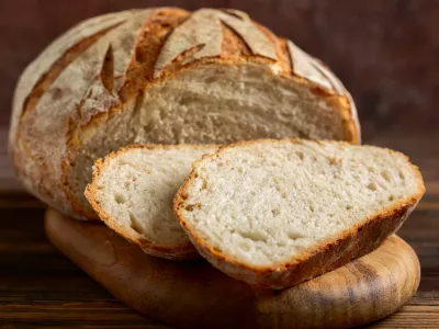 Golden crusty sourdough loaf with slices on wood board.