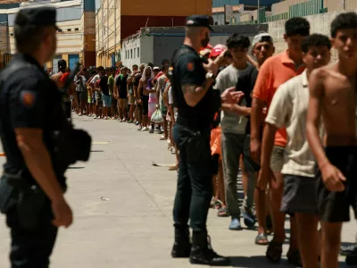 FILE PHOTO: Migrants queue to receive food staples from local NGO Media Luna Blanca in an industrial area where they are sleeping amid recent mass crossings by migrants on foot and by sea from Morocco into the Spanish territory, in Ceuta, Spain, August 6, 2026. REUTERS/Violeta Santos Moura/File Photo