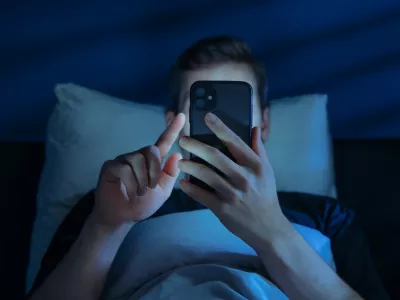 Close up of young man, alone in the dark bedroom, holds his smartphone close to face while scrolling social media or texting late at night. Screen dependence, excessive consumption of content / Foto: Arsenii Palivoda Getty Images