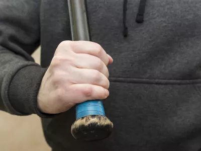 Powerful man's hand in a hoodie grips the shabby hilt of a black wooden baseball bat