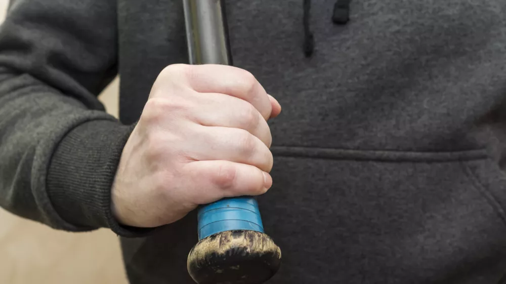 Powerful man's hand in a hoodie grips the shabby hilt of a black wooden baseball bat