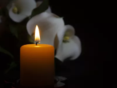 A close up of an orange candle and flame and lily flowers on a dark background.