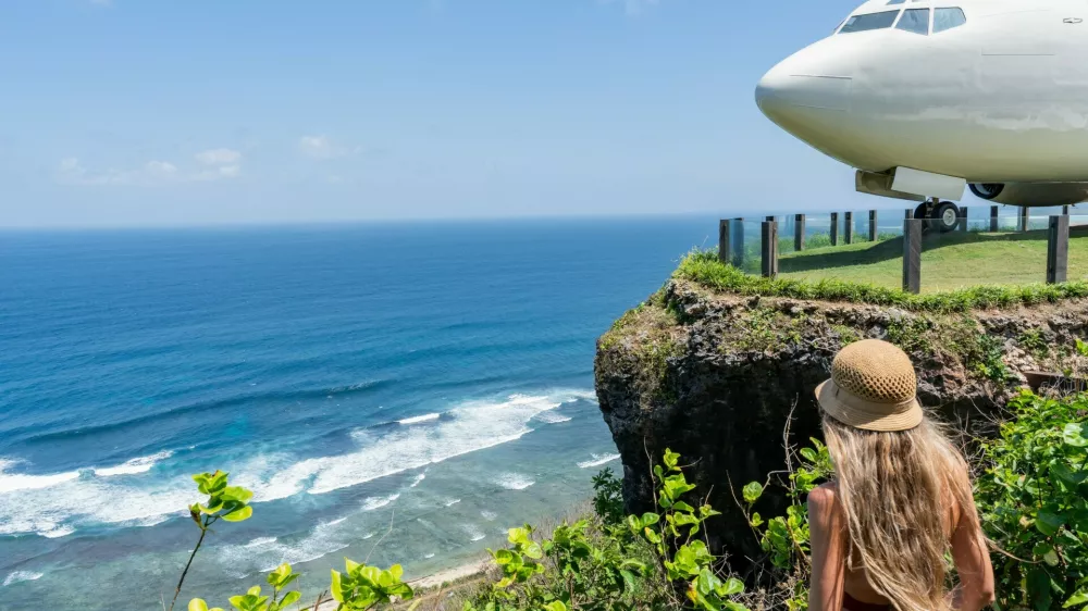 Blonde tourist admiring repurposed boeing 737 airplane on a cliff overlooking the indian ocean in bali,Image: 1001085464, License: Royalty-free, Restrictions:, Model Release: yes