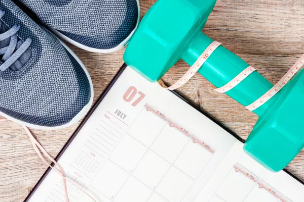 Calendar plan with green dumbbell and sneakers on wooden background. Workout plan concept. / Foto: Gam1983 Getty Images