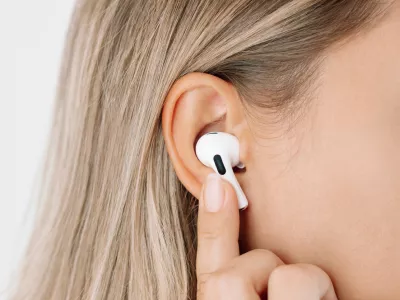 White wireless headphones for sports, running, cycling, walking in the ears of a young caucasian blonde woman listening to music. Close up. A girl switches songs or changes the volume with her finger / Foto: Marina Getty Images