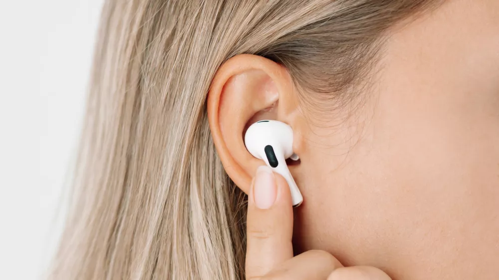 White wireless headphones for sports, running, cycling, walking in the ears of a young caucasian blonde woman listening to music. Close up. A girl switches songs or changes the volume with her finger / Foto: Marina Getty Images