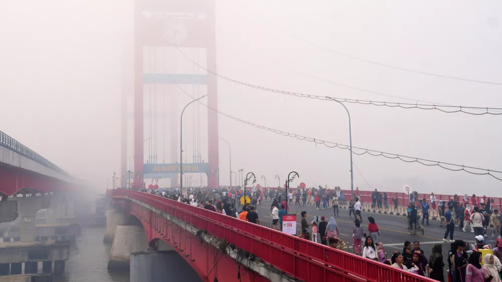 People walk along the Ampera Bridge as haze from wildfires blankets the city of Palembang, in South Sumatra, Indonesia, Sunday, Aug. 23, 2026. (AP Photo/Muhammad Fajri)